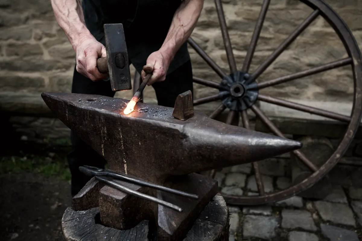 A smith working hot iron on an anvil.